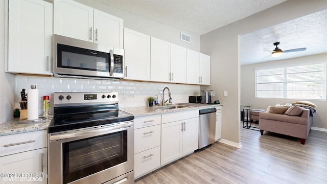 kitchen featuring appliances with stainless steel finishes, ceiling fan, light hardwood / wood-style floors, tasteful backsplash, and white cabinetry