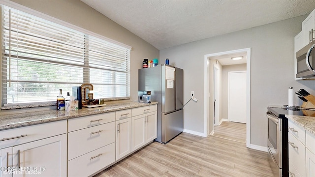 kitchen featuring light stone countertops, appliances with stainless steel finishes, light hardwood / wood-style floors, a textured ceiling, and white cabinets