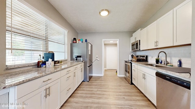 kitchen featuring white cabinets, backsplash, appliances with stainless steel finishes, sink, and light hardwood / wood-style floors