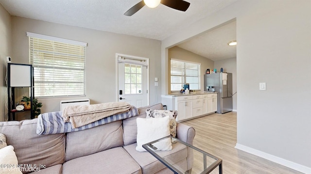 living room featuring lofted ceiling, light hardwood / wood-style flooring, ceiling fan, and a textured ceiling