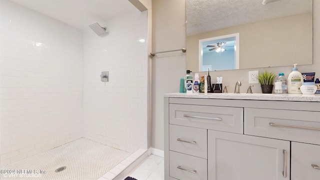 bathroom with tiled shower, ceiling fan, vanity, and a textured ceiling