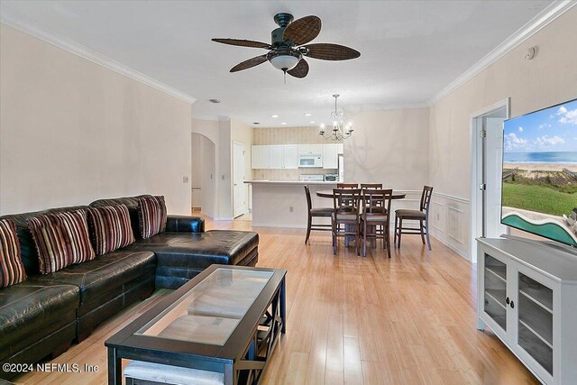 living room featuring ornamental molding, ceiling fan with notable chandelier, and light wood-type flooring