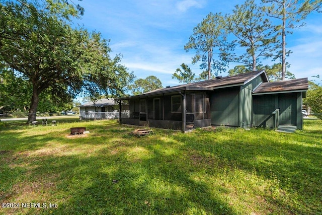 rear view of house with a fire pit, a yard, and a sunroom