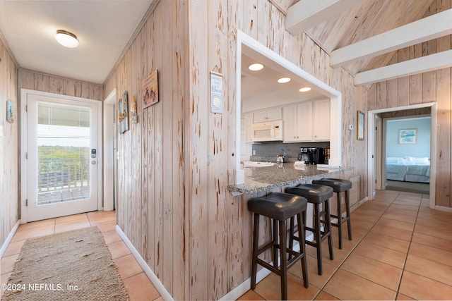 kitchen with light tile floors, dark stone counters, white cabinetry, and a breakfast bar area