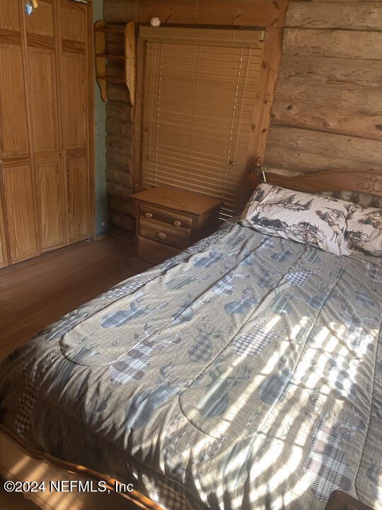 bedroom featuring log walls, wood-type flooring, and a closet