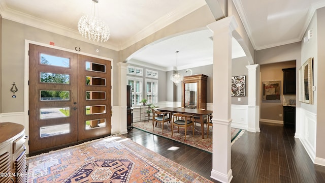 foyer entrance featuring an inviting chandelier, crown molding, ornate columns, and dark wood-type flooring