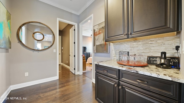 kitchen with light stone countertops, backsplash, dark wood-type flooring, dark brown cabinetry, and ornamental molding