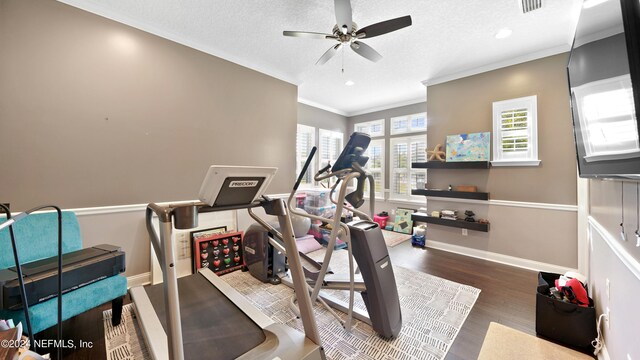 exercise area featuring a textured ceiling, ceiling fan, crown molding, and dark wood-type flooring