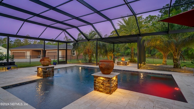 pool at dusk featuring pool water feature, a fire pit, glass enclosure, and a patio