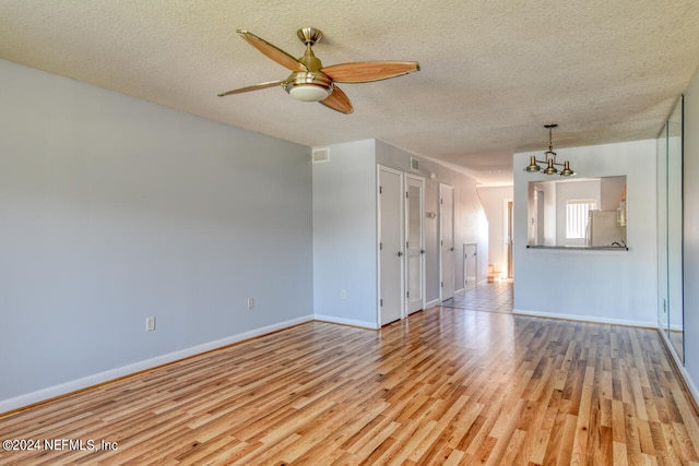 empty room featuring light hardwood / wood-style floors, ceiling fan with notable chandelier, and a textured ceiling