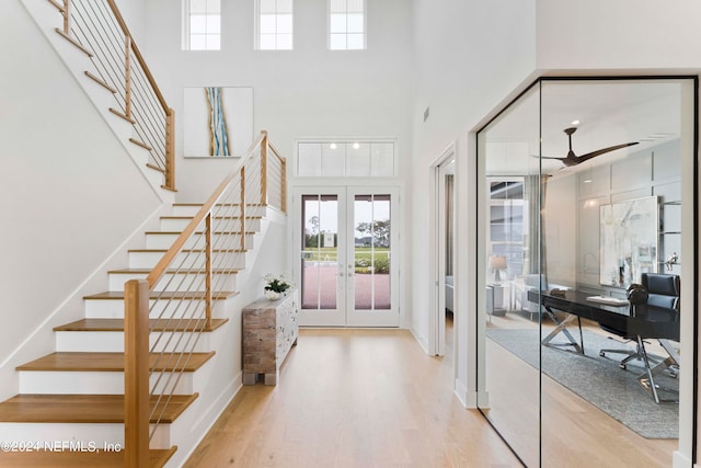 foyer with light hardwood / wood-style floors, french doors, and a towering ceiling