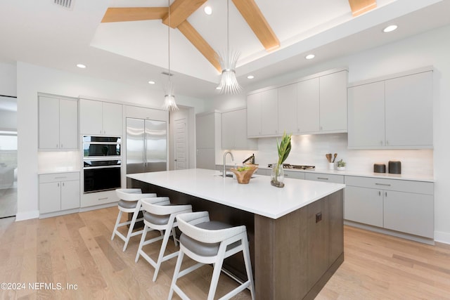 kitchen featuring tasteful backsplash, light hardwood / wood-style flooring, a kitchen island with sink, and appliances with stainless steel finishes