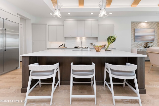 kitchen featuring a center island with sink, light hardwood / wood-style floors, stainless steel built in refrigerator, and decorative light fixtures