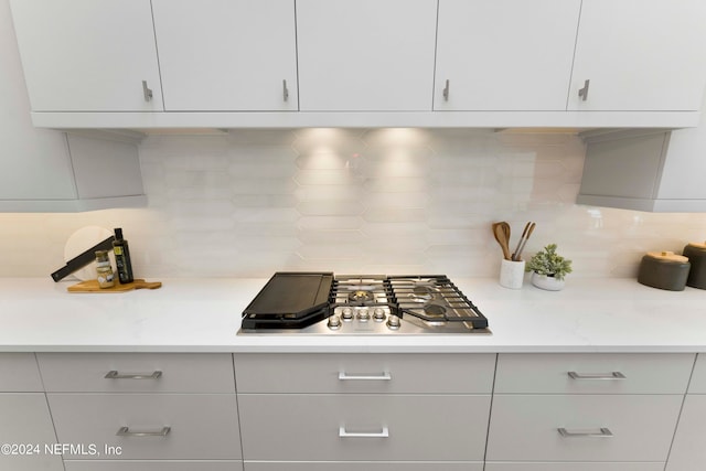 kitchen featuring white cabinets, light stone counters, backsplash, and stainless steel gas stovetop