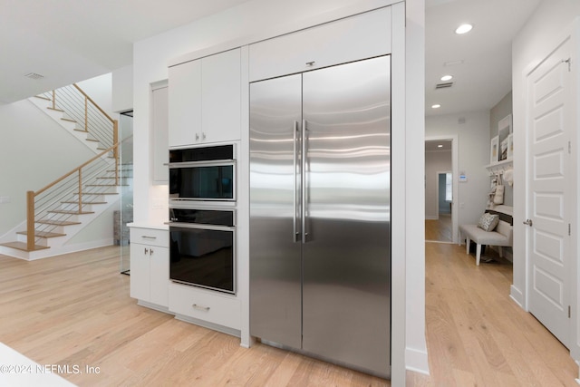 kitchen featuring oven, light hardwood / wood-style floors, built in fridge, and white cabinetry