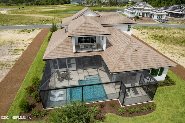 back of house with a water view, glass enclosure, and a lawn