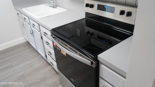 kitchen featuring white cabinets, sink, light hardwood / wood-style flooring, and stainless steel electric range oven