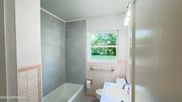 full bathroom with tiled shower / bath combo, tile walls, sink, toilet, and a textured ceiling