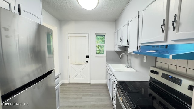 kitchen with appliances with stainless steel finishes, a textured ceiling, sink, light wood-type flooring, and white cabinetry