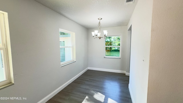 unfurnished room with a notable chandelier, plenty of natural light, dark hardwood / wood-style floors, and a textured ceiling