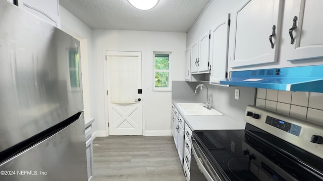 kitchen with appliances with stainless steel finishes, light hardwood / wood-style floors, wall chimney range hood, white cabinetry, and sink