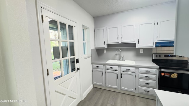 kitchen featuring electric stove, a textured ceiling, white cabinetry, sink, and light wood-type flooring