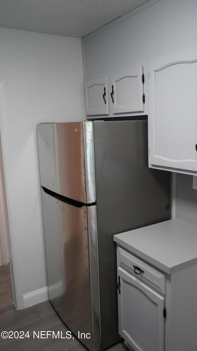 kitchen with dark hardwood / wood-style floors, stainless steel refrigerator, a textured ceiling, and white cabinetry