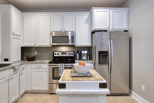 kitchen with white cabinets, light hardwood / wood-style floors, backsplash, and stainless steel appliances