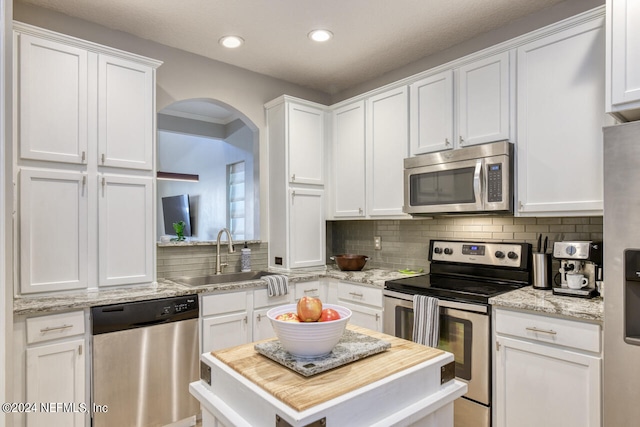 kitchen featuring white cabinets, light stone countertops, backsplash, appliances with stainless steel finishes, and sink