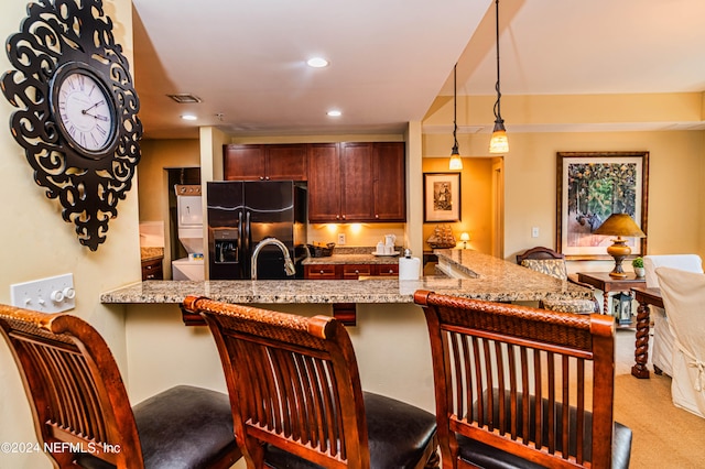 kitchen featuring black fridge with ice dispenser, a kitchen bar, decorative light fixtures, light stone counters, and sink