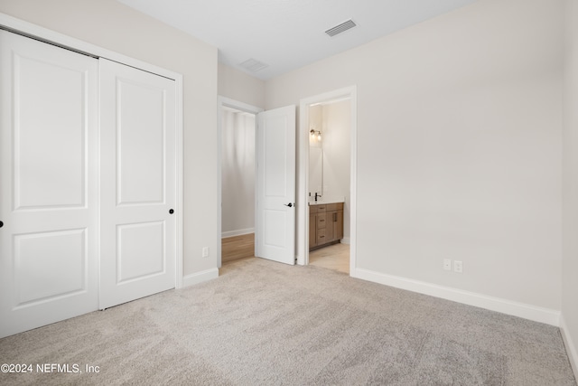 unfurnished bedroom with ensuite bathroom, a closet, and light colored carpet