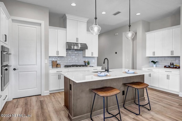 kitchen with pendant lighting, a kitchen island with sink, sink, light wood-type flooring, and white cabinetry