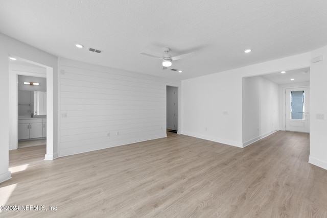 spare room with ceiling fan, light hardwood / wood-style flooring, a textured ceiling, and wooden walls