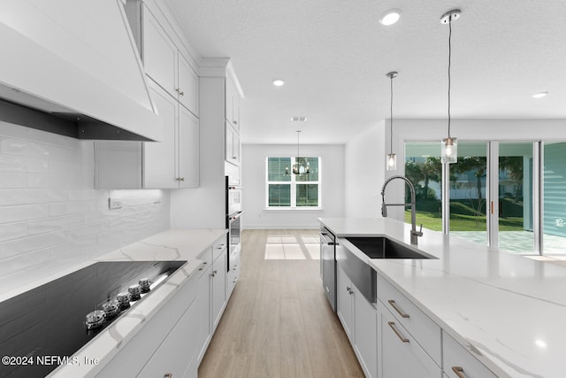 kitchen with premium range hood, white cabinets, light hardwood / wood-style flooring, light stone countertops, and decorative light fixtures