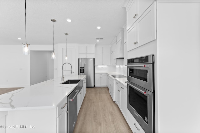 kitchen with white cabinetry, a large island, stainless steel appliances, pendant lighting, and light wood-type flooring