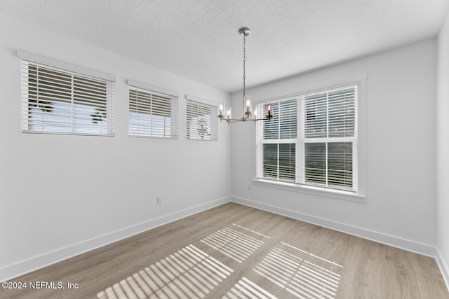 empty room featuring hardwood / wood-style flooring, a notable chandelier, and a textured ceiling