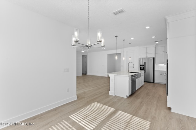 kitchen with light hardwood / wood-style floors, stainless steel appliances, hanging light fixtures, and an island with sink