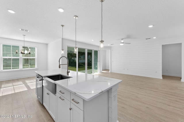 kitchen featuring a kitchen island with sink, white cabinets, pendant lighting, and light stone counters