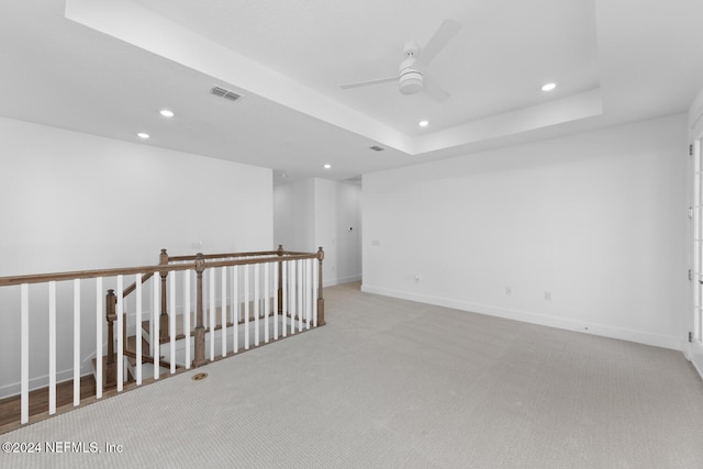 carpeted empty room with a raised ceiling and ceiling fan