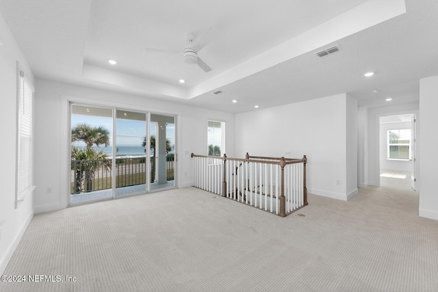 empty room with ceiling fan, a raised ceiling, and light carpet