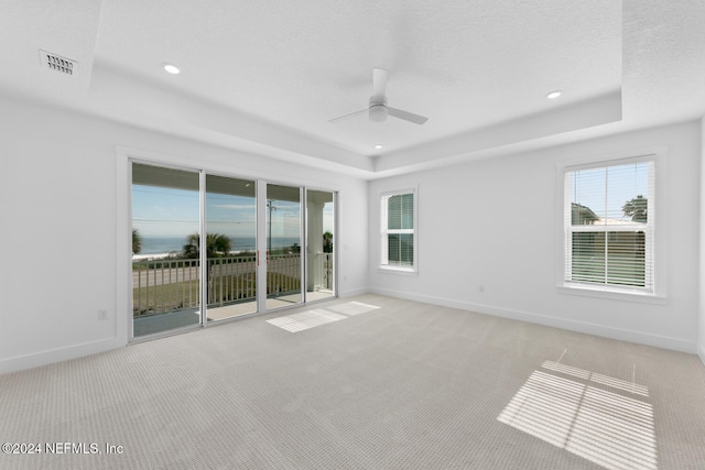 unfurnished room with a textured ceiling, ceiling fan, light carpet, and a tray ceiling