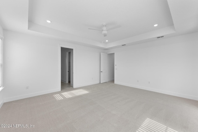 unfurnished room with a raised ceiling, ceiling fan, and light colored carpet