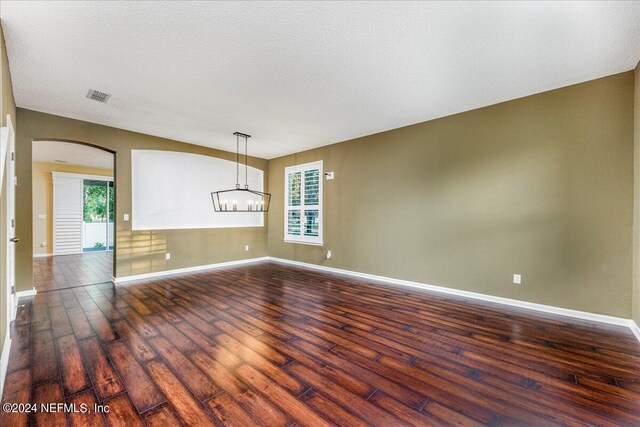 spare room with a textured ceiling, dark hardwood / wood-style floors, and an inviting chandelier