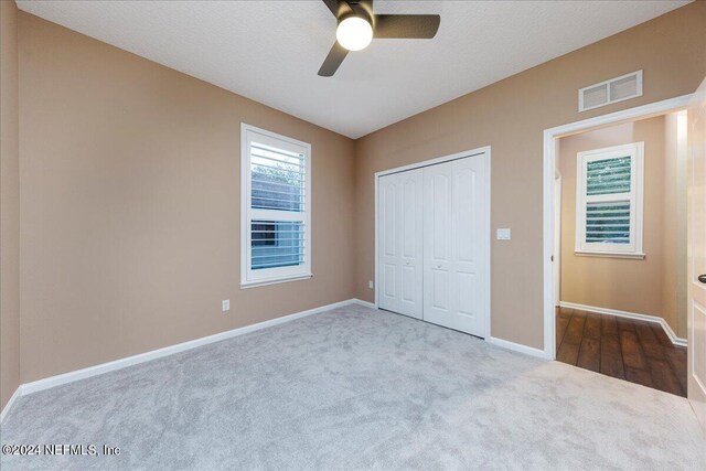 unfurnished bedroom featuring a closet, ceiling fan, a textured ceiling, and light colored carpet