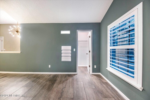 empty room featuring a notable chandelier, wood-type flooring, and a textured ceiling