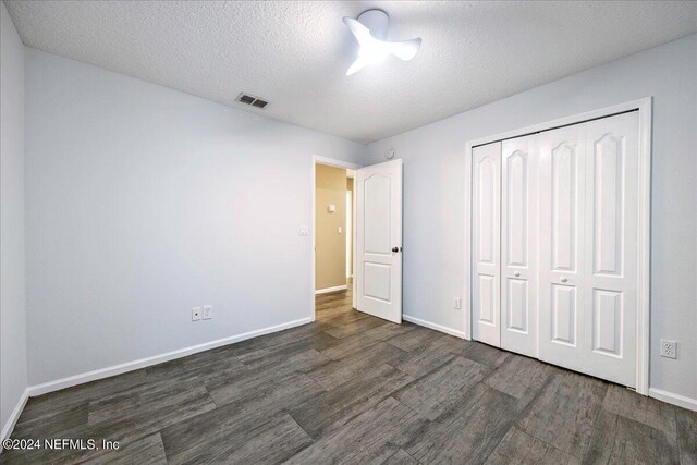 unfurnished bedroom featuring a closet, a textured ceiling, and dark hardwood / wood-style flooring