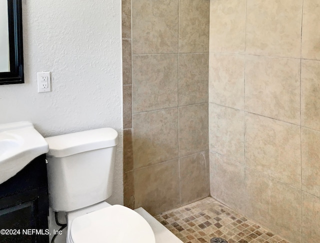 bathroom with tiled shower, toilet, and vanity