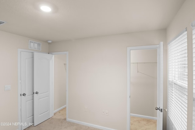 unfurnished bedroom featuring a walk in closet, light colored carpet, and a closet