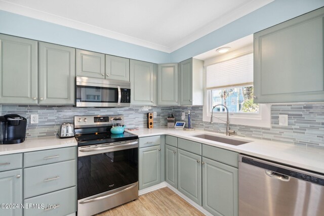 kitchen featuring appliances with stainless steel finishes, sink, light hardwood / wood-style floors, tasteful backsplash, and ornamental molding