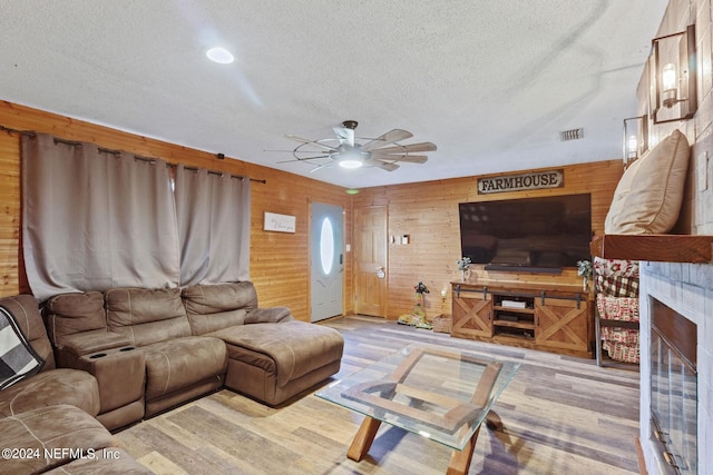 living room with light hardwood / wood-style floors, ceiling fan, wooden walls, and a textured ceiling